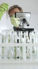 Male scientist wearing green protective gloves and mask is looking at green plant in test tube near...