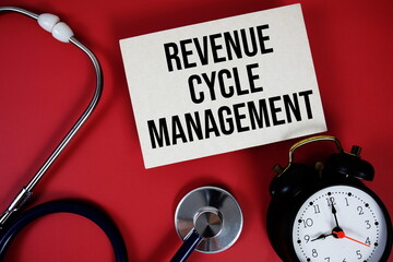 Revenue cycle management text written on paper card with stethoscope and alarm clock on red...