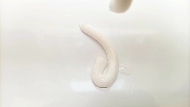 White cream texture face wash, shampoo, cleanser, cosmetic or skincare product dropping on white background, close up shot
