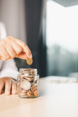 Hand places coin into saving jar, representing how smart finance, investment, banking practices turn money, cash, currency into financial wealth drives business growth and strengthens the economy.