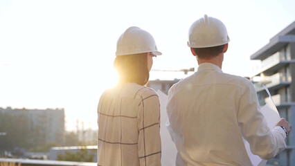Man and woman architects constructor engineers wearing safety glasses and hardhats, are examining...