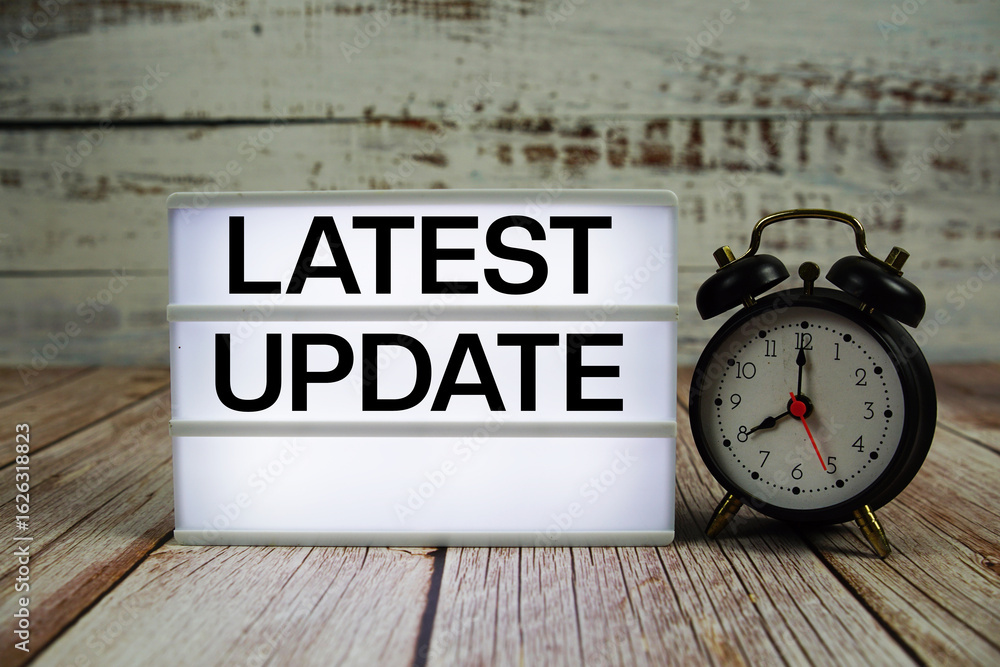 Poster latest update text on light box with alarm clock on wooden background