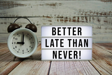 Better late than never! text on light box with alarm clock on wooden background