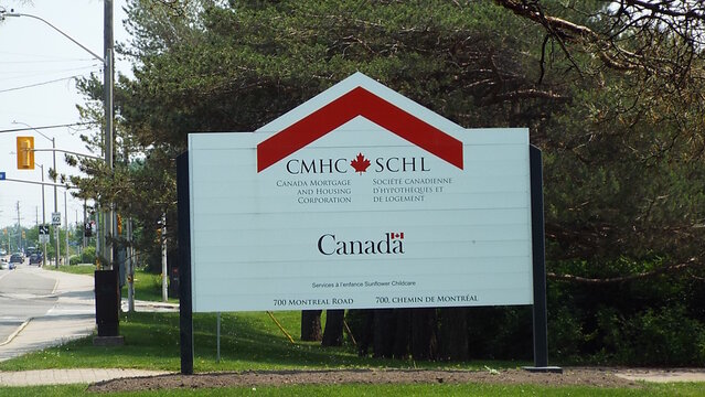 Ottawa, ON, Canada-July 25,2025: A white outdoor sign for CMHC SCHL (Canada Mortgage and Housing Corporation) with a red roofline graphic  at 700 Montr&eacute;al Rd.
