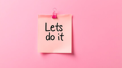 Motivational reminder note: "Lets do it!" pinned to pink background with paper clip. Positive message for action. Inspiring and encouraging message