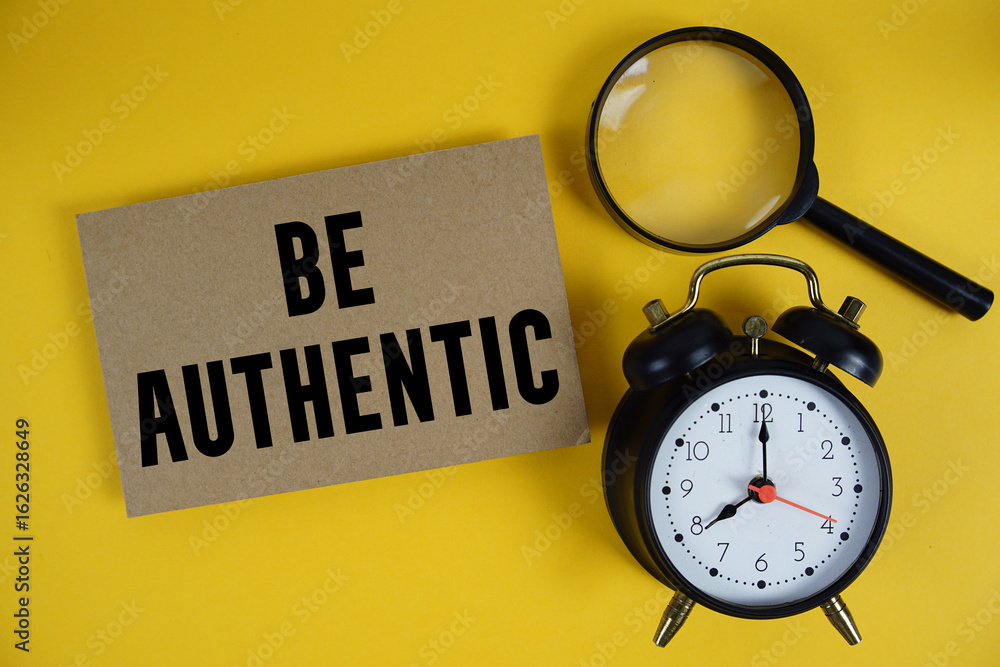 Poster be authentic text written on paper with magnifying glass and alarm clock on yellow background