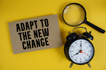 Adapt To The New Change text written on paper with magnifying glass and alarm clock on yellow...
