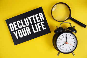 Declutter Your Life text written on paper with magnifying glass and alarm clock on yellow background