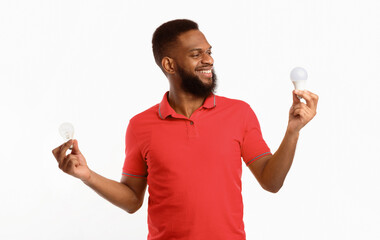 Save Energy. Happy African American Man Holding Two Light Bulbs Choosing Energy-Saving Lightbulb...