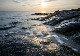 Fototapeta premium Coastal view of rocks and ocean water with the sun setting on the horizon, creating a serene and peaceful scene.