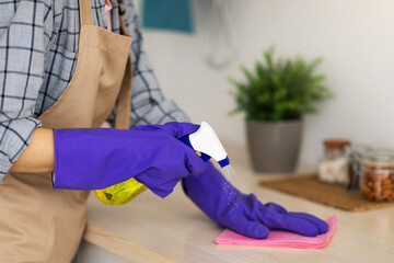 Unrecognizable housemaid with detergent cleaning kitchen table, closeup of hands. Young woman doing...