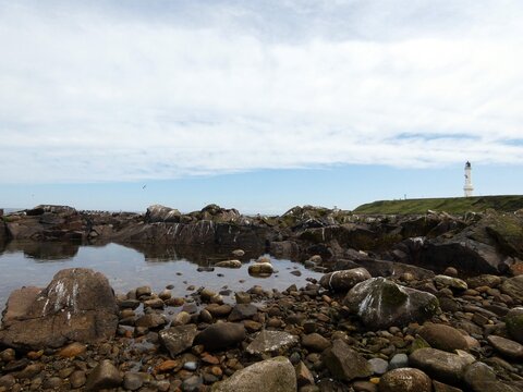 Scenic coastal view featuring rocky shoreline with white lighthouse - Powered by Adobe