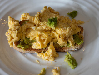 Scrambled eggs with avocado on toasted whole grain bread at a breakfast table