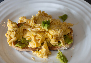 Scrambled eggs with avocado on toasted whole grain bread at a breakfast table