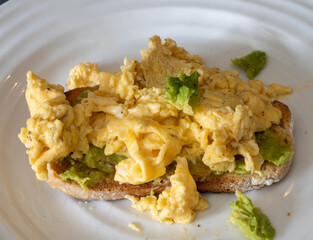 Scrambled eggs with avocado on toasted whole grain bread at a breakfast table