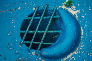 Close-up of a round grated opening in a weathered blue metal surface, showing rust, peeling paint, and textured detail.