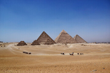 Pyramids of Giza and camel caravan in ancient desert landscape under clear blue sky