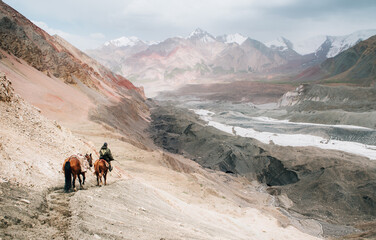 Beautiful picturesque wide angle Pamir mountains valley shot with horsemen heading by dusty...