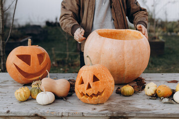 Making a jack o lantern. Hands carving halloween pumpkin on rustic wooden table in autumn garden,...