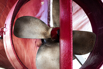 Detailed view of a marine propeller enclosed in a red-painted nozzle, showing texture, rust, and...