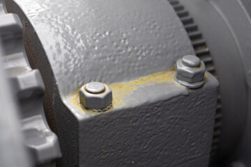 Macro view of two industrial bolts on a rough, painted gray metal surface with signs of grime and...