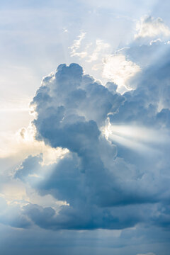 Dramatic cumulus clouds illuminated by sunlight. Bright rays of sunshine pierce through the cloudscape, creating a serene and majestic sky scene.
