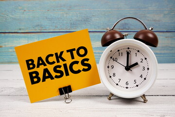 Back To Basics text written on paper card with alarm clock on wooden background