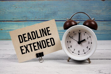 Deadline Extended text written on paper card with alarm clock on wooden background