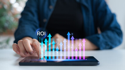 Hand touching tablet screen with ROI and uptrend graph. Concept of return on investment, digital...