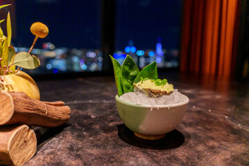 Fresh oyster on crushed ice topped with wasabi and avocado mousse, served in a ceramic bowl with...
