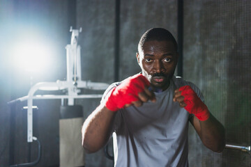 Workout in gym. African man fighter ready for fight punching with boxing wraps protective bandages to camera. Strong man training punches looking concentrated straight preparing for boxing sparring