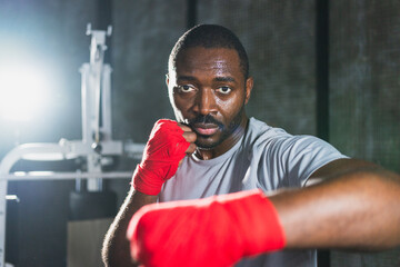Workout in gym. African man fighter ready for fight punching with boxing wraps protective bandages to camera. Strong man training punches looking concentrated straight preparing for boxing sparring