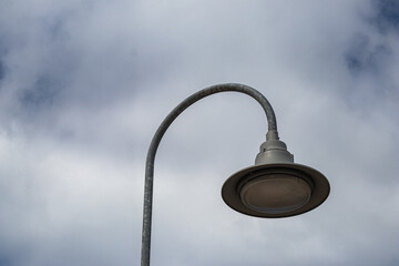 Close-up of a curved metal street lamp with an overcast sky background, showing minimalistic and...