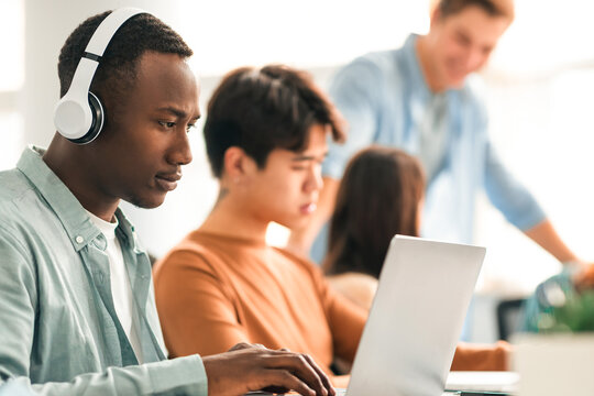 Management And Marketing Concept. Diverse group of busy multicultural colleagues sitting at table working on business project at boardroom, selective focus on African American man in headset using pc