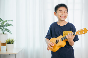 A young boy in a blue shirt plays a yellow ukulele, smiling with joy in the living room. The white...