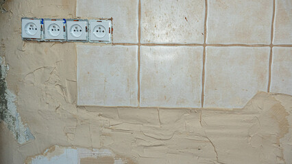Poor-quality wall renovation with uneven plaster, misaligned ceramic tiles, and exposed electrical outlets, showing unfinished and unprofessional DIY home repair work.