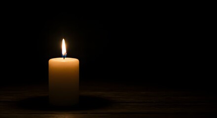 A lit wax candle with a bright flame casting a soft glow in a dark and shadowy environment setting mood