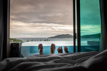 Foot view of honeymoon couple lying on bed under white blanket. Morning in bedroom by the window...