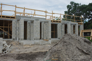 Concrete Block House Under Construction at an Active Building site with materials and framing visible amidst sandy ground, embodying progress and development. Pile of dirt in front
