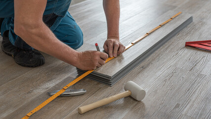 Floating floor work. The worker measuring the board of vinyl plank before shortening.