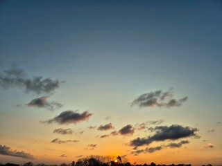 Beautiful sunset sky with scattered clouds and silhouette trees on the horizon