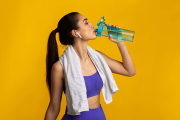 Active Lifestyle. Sporty young lady with white towel on neck drinking mineral water from the...