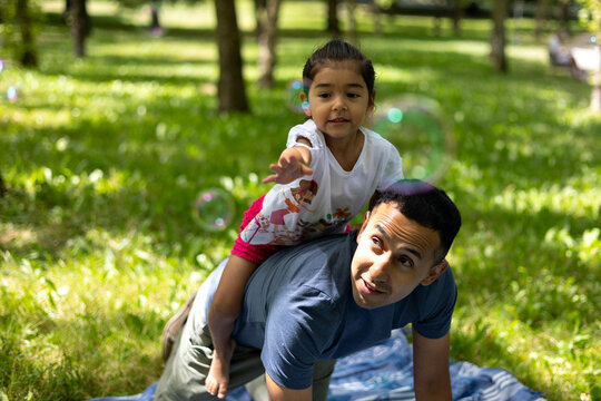 Latin father and daughter having fun with soap bubbles in a green park