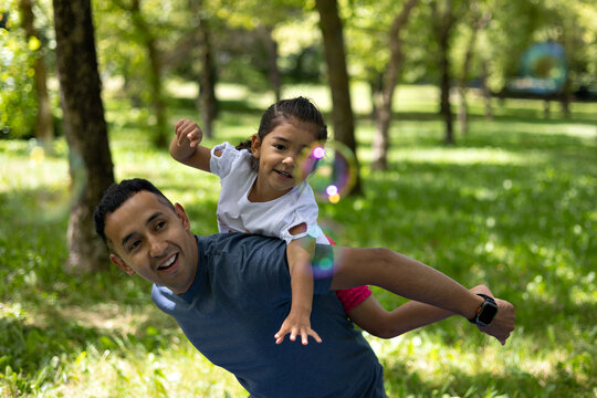 Latin father and daughter having fun in a park playing with soap bubbles - Powered by Adobe