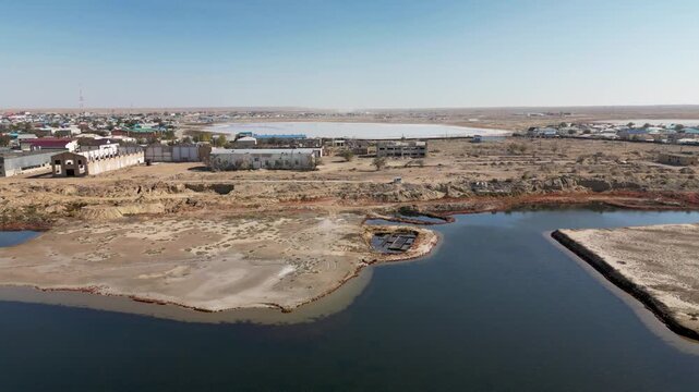 Aerial view of Aralsk town near the former shoreline of the Aral Sea. Only a narrow water channel remains where the Aral Sea once reached, surrounded by dusty plains.