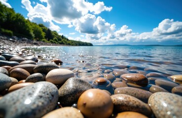 A scenic view of a pebble beach along a calm lake under a bright blue sky with fluffy clouds