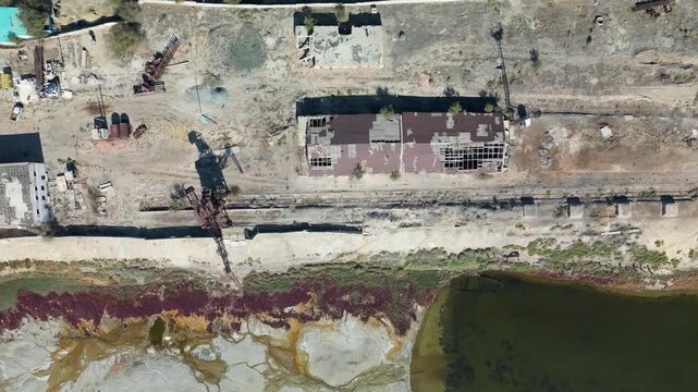 Top-down aerial shot of Aralsk&rsquo;s industrial zone: a rusted crane, old rail lines and a narrow canal cutting through the former shoreline of the Aral Sea.