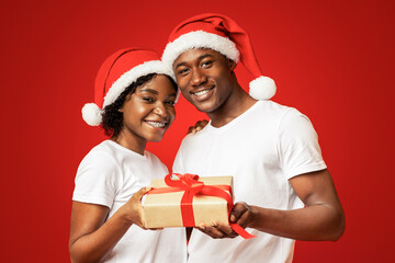 Cheerful african american couple celebrating New Year together, wearing Santa hats, embracing,...