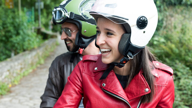 Happy couple riding scooter wearing helmets - Powered by Adobe