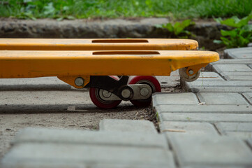 A yellow pallet jack stands on a concrete and brick surface with a backdrop of lush green grass,...